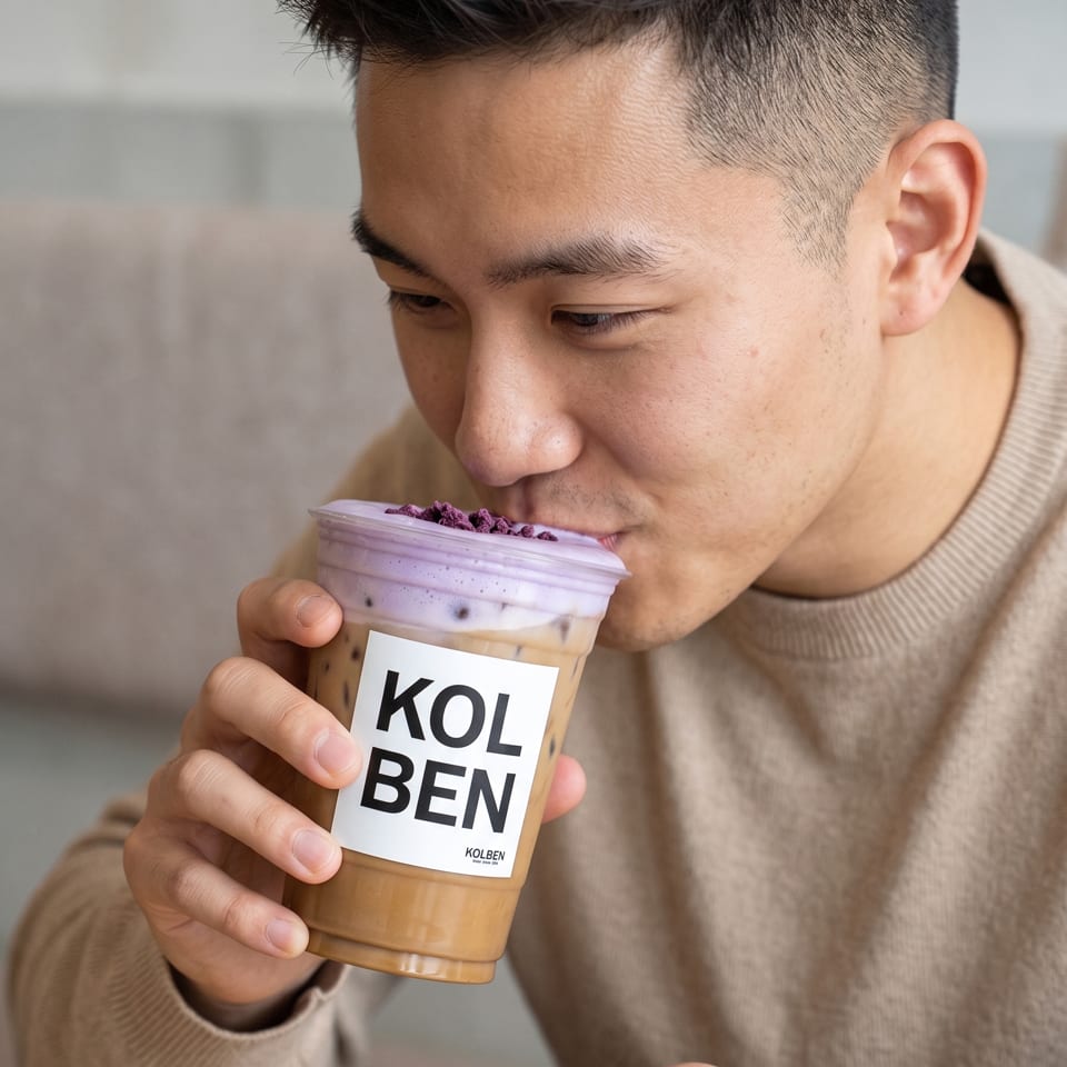 A man sips a Kolben iced coffee with purple foam and sprinkles from a clear cup.