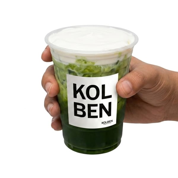 Hand holding a Kolben branded cup with a green drink topped with white cream.